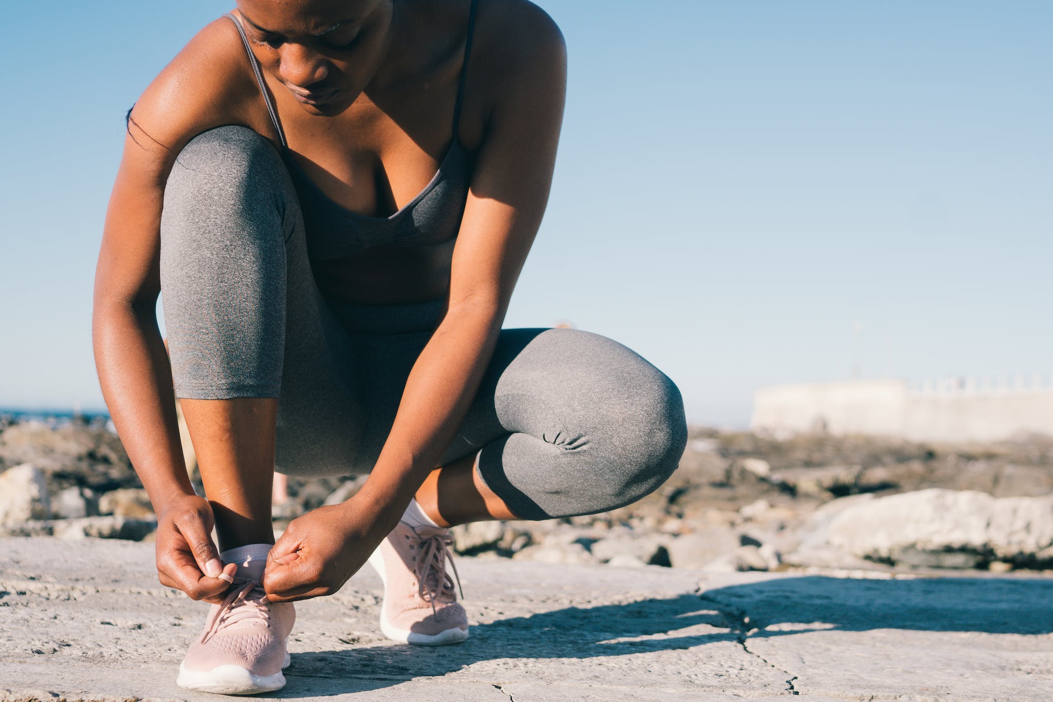 Close-up Photo of Woman in Gray Tank Top and Gray Leggings Tying Her Shoes